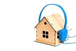 Blue headphones put on a miniature wooden house model isolated on white background. House noise and acoustic insulation concept.