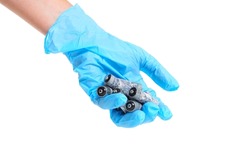 Close-up of a human hand in a blue nitrile glove holding a bunch of heavily corroded AA type batteries isolated on white background.