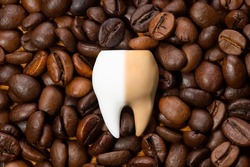 Large half-white and half-brown tooth on a pile of roasted coffee beans. Coffee staining and teeth whitening concept.