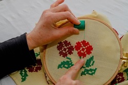 Woman choosing green yarn for her patterns while doing cross-stitch. Cross-stitch art. Hand Mader. Etamine.