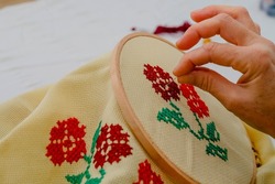 Woman doing cross-stitch with red floral patterns. Cross-stitch art. Hand Mader. Etamine.