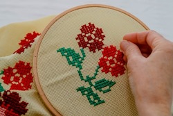 Woman doing cross-stitch with red floral patterns. Cross-stitch art. Hand Mader. Etamine.