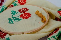 Woman doing cross-stitch with red floral patterns. Cross-stitch art. Hand Mader. Etamine. Yellow thread.