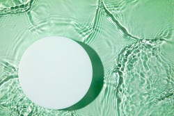 Empty white circle podium on transparent clear green calm water texture with splashes and waves in sunlight. Abstract nature background for product presentation. Flat lay cosmetic mockup, copy space.