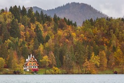 house by lake, autumn forest and mountains with colorful fall trees