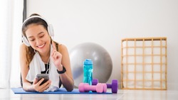 Asian woman listening to music with headphone and smartphone after play yoga and exercise at home background with copy space.Exercise for Lose weight, increase flexibility And tighten the shape.