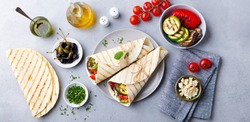 Wrap sandwich with grilled vegetables and feta cheese on a plate. Grey background. Top view.
