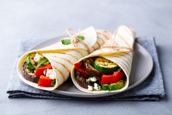 Wrap sandwich with grilled vegetables and feta cheese on a plate. Grey background. Close up.