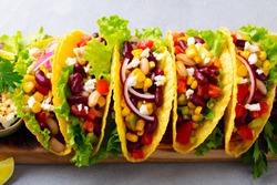 Taco with mixed vegetables, beans on cutting board. Grey background. Close up.