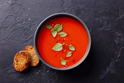 Tomato soup with basil in a bowl. Dark background. Close up. Top view.