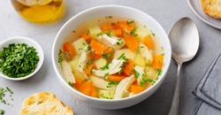 Chicken soup with vegetables in white bowl. Grey stone background. Close up.