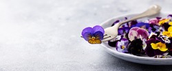 Edible flowers, field pansies, violets on white plate. Grey background. Copy space.