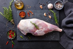 Raw lamb leg with spices and herbs on marble cutting board. Dark background. Top view.