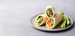 Wrap sandwich, roll with fish salmon and vegetables. Grey background. Close up. Copy space.