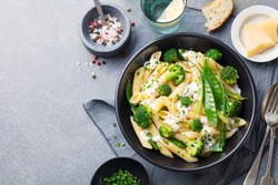 Pasta with green vegetables and creamy sauce in black bowl on grey stone background. Top view. Copy space.