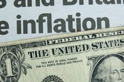 A US one dollar bill lying below a newspaper headline news on inflation. Concept for the dollar buying power amidst rising goods prices due to shortages and increasing demand. Closeup macro view.