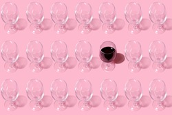 Glass pattern. Repeating empty wine glass on pink background.One glass filled with wine. Abstract background.