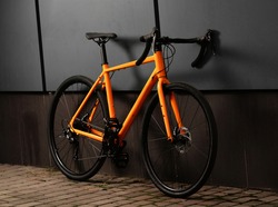 Gravel bicycle. Shiny orange bike for offrad cycling on grey background. Close up.