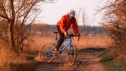 A cyclist on a gravel bike rides along the road raising dust from the rear wheel at sunset. Gravel biking. Extreme sports and activity concept.