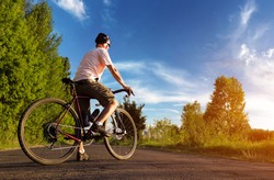Cyclist stands on the road at sunset. Beautiful landscape of a man with road bike against the blue sky. Sports lifestyle.