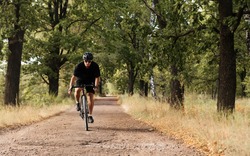 Young male cyclist in a helmet and glasses rides a bicycle on the countryside road. Athletic guy on a gravel bike enjoys training on fresh air.
