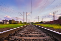 Railroad in motion with motion blur effect at sunset with beautiful sky and purple clouds. Railway transportation.