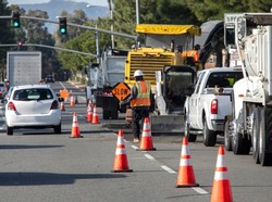 Wide view of raod construction site and a nan holding traffic sign that says SLOW .Bright orange traffic cones and trucks and cars are visible