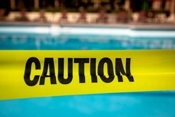 Yellow caution tape at a resort style pool preventing access or use of the pool for contamination or an investigation