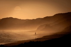 Silhouette of one person at San Onofre State beach at sunset with aj hazy sun in the background. 