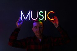 Hipster handsome man by neon signs. Multicolored neon sign music. Party concept. Modern style. Neon sign.