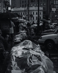 Black and white photo of a street market under the rain. People under the umbrellas in the background. Street photography concept, wet goods on market.
