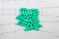 green pills in the form of capsules on the background of a cardiogram. Medical concept. Cardiovascular diseases. Heart treatment.