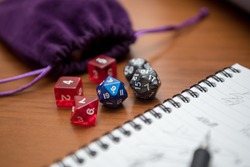 Set of pen, notebook, and dices to play role game like dungeons and dragons. Close up photography, purple bag to storage the dices.