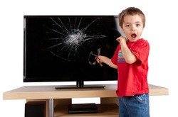 Shocked little boy holding a slingshot standing in front of a TV with broken screen. Home insurance concept. Studio shot isolated on white background.