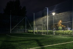 An amateur football field illuminated at night. A small football field lit by lanterns in the evening. Green football field illuminated at night. Soccer field in night with spotlight