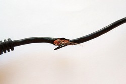 Damaged black electric cord on white background. Dangerous broken power electrical cable