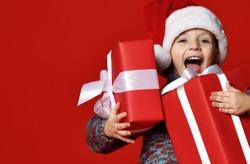 Funny smiling joyful  child boy in Santa red hat holding Christmas gift in hand over the red background