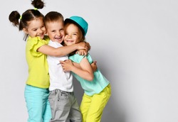 Studio portrait of children on a light background: full body shot of three children in bright clothes, two girls and one boy. Triplets, brother and sisters. hugging on camera. Family ties, friendship.