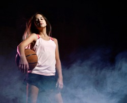 Portrait of young female basketball player passing the ball. Beautiful caucasian woman in sportswear playing basketball on grey background with smoke effect