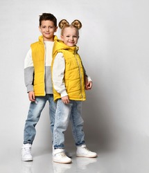 teenage boy and girl posing against a light background, children are dressed in yellow puffy sleeveless zipper vests and jeans. urban teen fashion