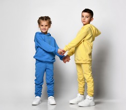 Two children in stylish bright sports suits sitting holding hands on a white background. Cute little boy and girl posing in the studio showcasing a new collection of sportswear for children.