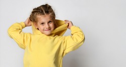 Portrait of a joyful active little girl wearing a hood on a white background. Happy cute child in a yellow sports hoodie white background. Sportswear advertising concept. Banner.