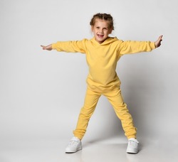 Full length portrait of a little girl dressed in a bright yellow sports suit. Cute child posing on a white background with outstretched arms. Concept of active childhood.