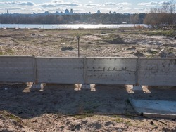 The panoramic view over the construction site behind the concrete fence at the bank of the Dnipro river and the right bank of Kyiv at the horizon.