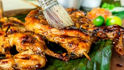 Applying marinade to juicy barbecued chicken with a brush. It is Chicken Inasal, a popular grilled dish in the Philippines.
