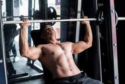 Working out and training scene - A shirtless asian 40 year old fit male does incline bench presses on a Smith Machine.