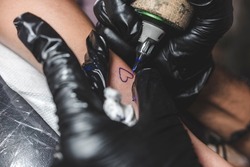 A professional tattoo artist outlines a small heart shape with a rotary tattoo machine equipped with a round liner cartidge.