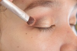 Applying eyeshadow shimmer on the upper eyelid of a young asian lady with a domed brush. Makeup artist techniques.