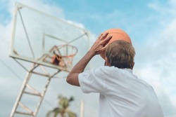 An older basketball player shoots some hoops outdoors. Great free throw shooting form even in old age. Using a weathered basketball.