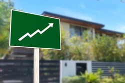 A sign showing an upward arrow in front of a gated house. Concept of increasing home prices and value or a real estate boom.